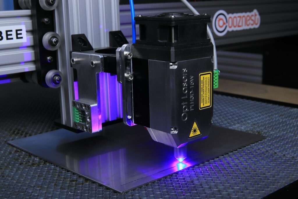 Laser engraving machine with a blue laser emitting from its nozzle onto a metal surface. It showcases advanced technology for precision cutting.